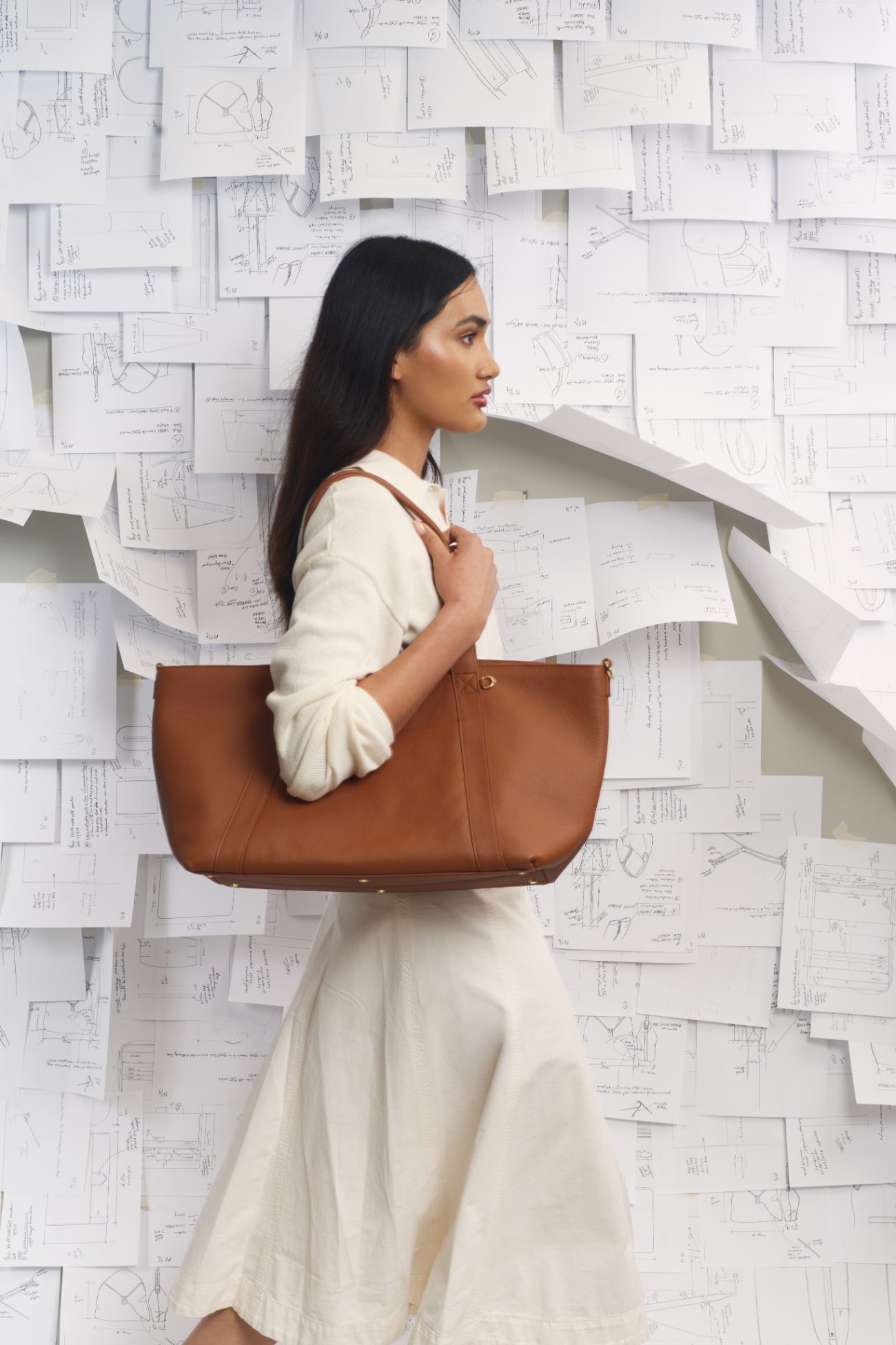 Leatherology leather tote carried against a wall of design sketches